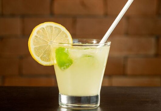 Copo de caipirinha de limão com gelo e limões frescos