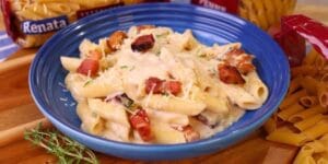 Macarrão cremoso com bacon, frango e queijo servido em prato raso.