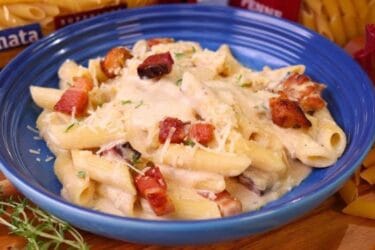 Macarrão cremoso com bacon, frango e queijo servido em prato raso.
