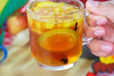 Quentão tradicional servido em copo, com frutas e especiarias.