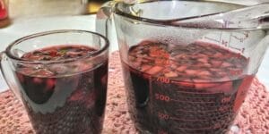 Vinho quente servido em copo, com canela e cravo.