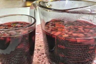 Vinho quente servido em copo, com canela e cravo.