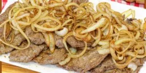 Bife acebolado dourado com cebola caramelizada servido em prato branco