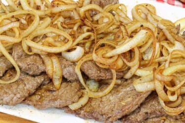 Bife acebolado dourado com cebola caramelizada servido em prato branco