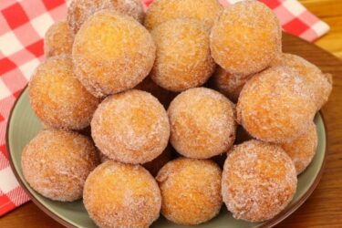 Cesta de vime cheia de bolinho de chuva com massa de banana, polvilhados com açúcar e canela, ao lado de uma xícara de café