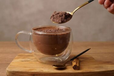 Caneca de cappuccino caseiro com muita espuma e polvilhado com canela ao lado do pote com a mistura em pó.