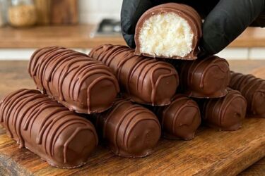 Fileira de bombons de prestígio caseiro cortados ao meio, mostrando o recheio de coco bem branquinho e a casquinha de chocolate brilhante.