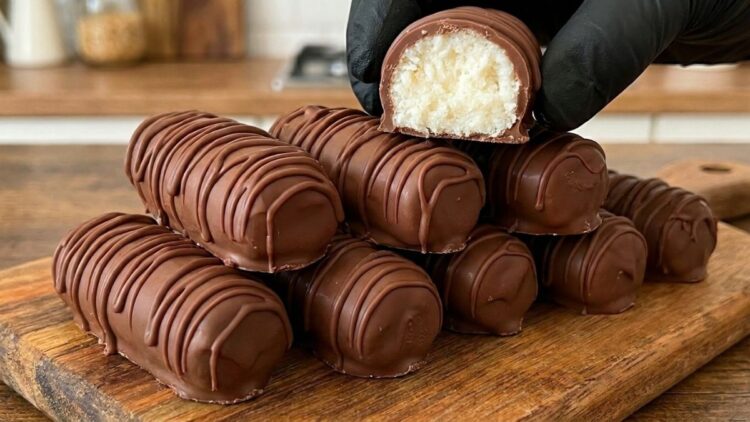 Fileira de bombons de prestígio caseiro cortados ao meio, mostrando o recheio de coco bem branquinho e a casquinha de chocolate brilhante.