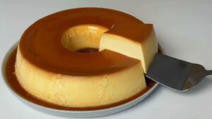 Pudim 4 leites bem dourado e brilhante em um prato, com muita calda de caramelo escorrendo pelas laterais.