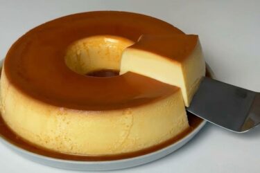 Pudim 4 leites bem dourado e brilhante em um prato, com muita calda de caramelo escorrendo pelas laterais.