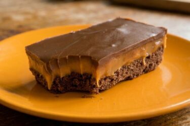Quadrados da torta de manteiga escocesa do Pica-Pau, mostrando a base de chocolate, o recheio de caramelo espesso e o topo de chocolate ao leite brilhante.