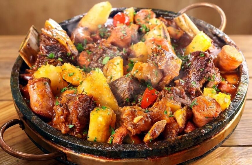 Saiba quais são as melhores carnes para cozinhar na panela de pressão 3 Panela de ferro servindo vaca atolada fumegante com pedaços de costela, mandioca macia, rodelas de linguiça e tomates-cereja por cima.