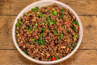 Panela com carne moída refogada bem soltinha e brilhante, salpicada com cheiro-verde fresco por cima.