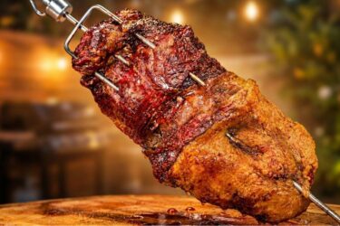 Peça de fraldinha assada no espeto sendo fatiada, mostrando a casquinha de gordura dourada e o interior rosado e suculento da carne. fraldinha no espeto