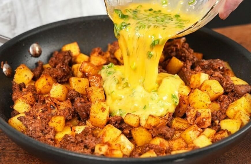 Fatia de torta de frigideira de batata com carne moída, mostrando o queijo derretido no topo com cebolinha e o recheio denso de carne e cubinhos de batata dourada.