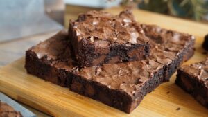 Quadrado de brownie trufado com a casquinha craquelada e brilhante por cima, mostrando o miolo escuro, denso e super molhadinho com pedaços de chocolate.