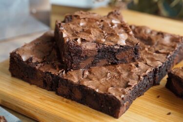 Quadrado de brownie trufado com a casquinha craquelada e brilhante por cima, mostrando o miolo escuro, denso e super molhadinho com pedaços de chocolate.