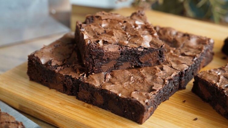 Quadrado de brownie trufado com a casquinha craquelada e brilhante por cima, mostrando o miolo escuro, denso e super molhadinho com pedaços de chocolate.