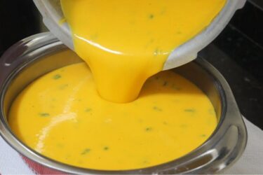 Prato fundo de cerâmica com caldo de batata com cenoura bem cremoso e alaranjado, finalizado com cheiro-verde picadinho e acompanhado de fatias de pão.