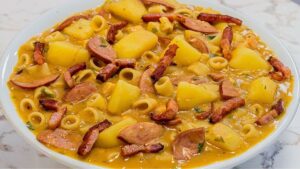 Prato fundo com sopa de feijão bem cremosa e grossa, com rodelas de calabresa, cubos de batata, macarrão e cheiro-verde, salpicada com bacon crocante.