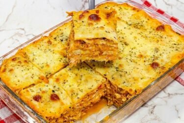 Travessa de vidro com lasanha de frango cremosa recém-assada, mostrando o queijo muçarela gratinado e dourado por cima com ervas.