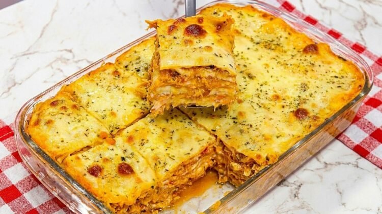 Travessa de vidro com lasanha de frango cremosa recém-assada, mostrando o queijo muçarela gratinado e dourado por cima com ervas.
