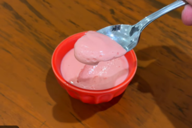Potinhos individuais com Danoninho caseiro cremoso de morango, mostrando a textura aveludada em uma colher.