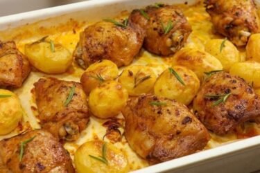 Assadeira com sobrecoxa de frango assada no forno com pele crocante e dourada, acompanhadas de batatas coradas e alecrim.