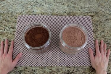 Dois potes na bancada da cozinha, um com chocolate em pó escuro e outro com achocolatado claro