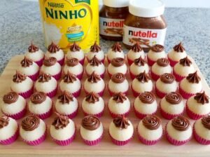 Brigadeiros de leite Ninho dispostos em forminhas, cobertos com leite em pó e decorados com rosetas de Nutella no topo.