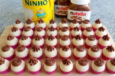 Brigadeiros de leite Ninho dispostos em forminhas, cobertos com leite em pó e decorados com rosetas de Nutella no topo.