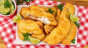 Travessa com filés de peixe frito na cerveja bem dourados e crocantes, acompanhados de fatias de limão.