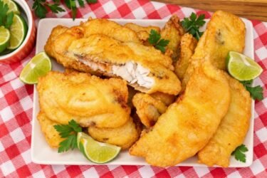 Travessa com filés de peixe frito na cerveja bem dourados e crocantes, acompanhados de fatias de limão.