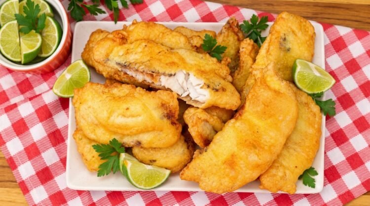 Travessa com filés de peixe frito na cerveja bem dourados e crocantes, acompanhados de fatias de limão.