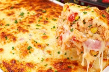 Travessa de vidro com arroz de forno completão recém-assado, mostrando o queijo muçarela gratinado e dourado por cima com orégano.