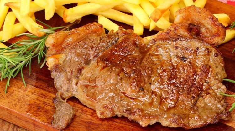 Como Fazer Bife de contrafilé grelhado fatiado em uma tábua de madeira, mostrando a carne rosada e suculenta no centro.