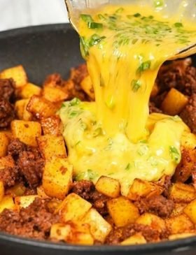 Fatia de torta de frigideira de batata com carne moída, mostrando o queijo derretido no topo com cebolinha e o recheio denso de carne e cubinhos de batata dourada.