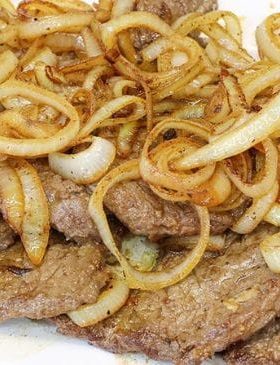 Bife acebolado dourado com cebola caramelizada servido em prato branco