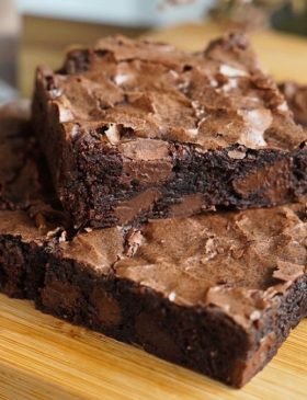 Quadrado de brownie trufado com a casquinha craquelada e brilhante por cima, mostrando o miolo escuro, denso e super molhadinho com pedaços de chocolate.