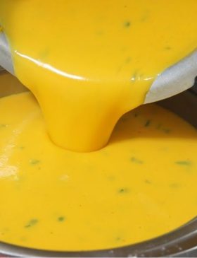 Prato fundo de cerâmica com caldo de batata com cenoura bem cremoso e alaranjado, finalizado com cheiro-verde picadinho e acompanhado de fatias de pão.
