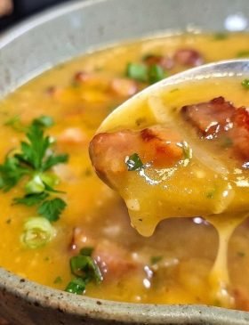 Tigela cheia de caldo de mandioca com bacon e calabresa fumegante, decorada com cheiro-verde picadinho por cima.