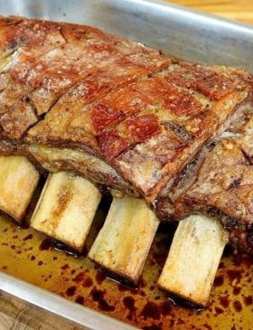 Pedaço de costela assada no forno com papel-alumínio, dourada por cima e soltando do osso.