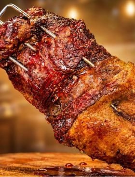 Peça de fraldinha assada no espeto sendo fatiada, mostrando a casquinha de gordura dourada e o interior rosado e suculento da carne. fraldinha no espeto