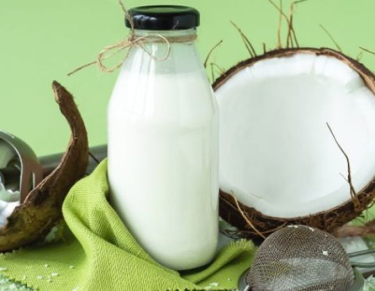 Garrafa de leite de coco ao lado de cocos partidos