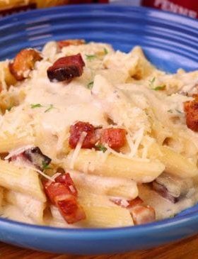 Macarrão cremoso com bacon, frango e queijo servido em prato raso.