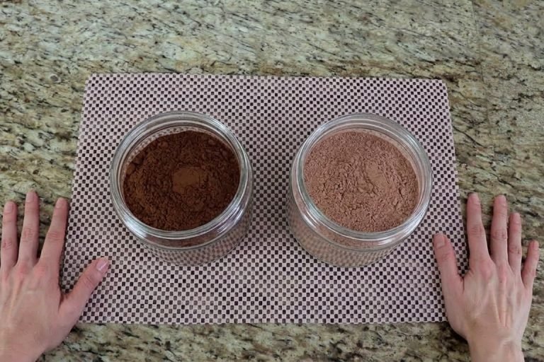 Chocolate em pó x achocolatado qual usar nas receitas Dois potes na bancada da cozinha, um com chocolate em pó escuro e outro com achocolatado claro
