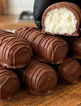 Fileira de bombons de prestígio caseiro cortados ao meio, mostrando o recheio de coco bem branquinho e a casquinha de chocolate brilhante.