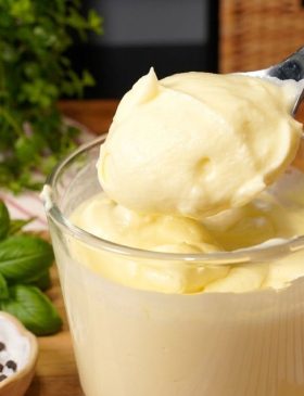 Pote de vidro com requeijão caseiro branco e cremoso, com uma faca passando em uma torrada ao lado.