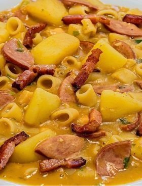 Prato fundo com sopa de feijão bem cremosa e grossa, com rodelas de calabresa, cubos de batata, macarrão e cheiro-verde, salpicada com bacon crocante.