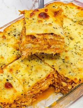 Travessa de vidro com lasanha de frango cremosa recém-assada, mostrando o queijo muçarela gratinado e dourado por cima com ervas.